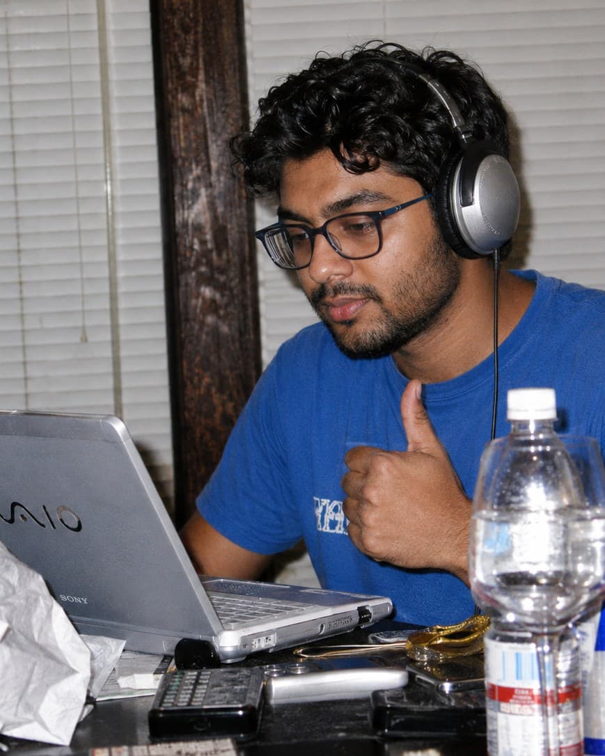 Pranav Jha at a laptop, headphones on, giving a thumbs up mid-build